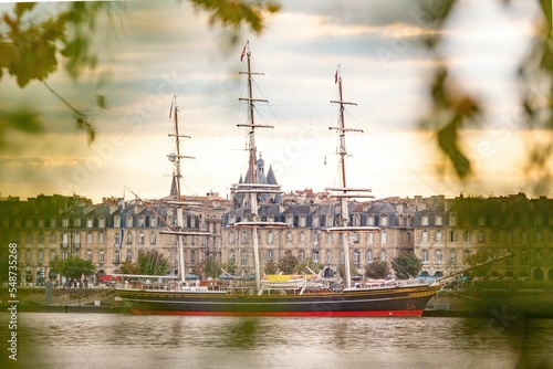 Fototapeta Moored sailing ship with city buildings in the background