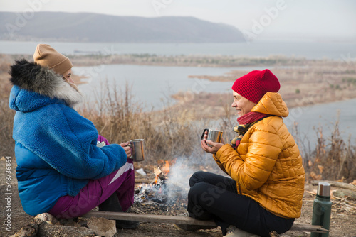 two female friends drink tea sitting near a bonfire in the fall in nature. mental health. Slow life. Enjoying the little things. Lykke concept  photo