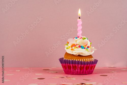 Birthday cupcake with candle light on a pink background. Cake with whyte cream and confectionery decor. Festive dessert and congratulations. Happy Birthday. photo