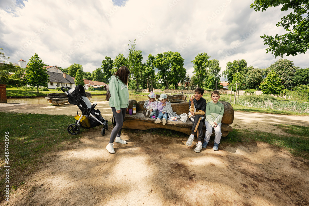 Obraz premium Mother with kids sitting and having rest in wooden bench outdoor in park.
