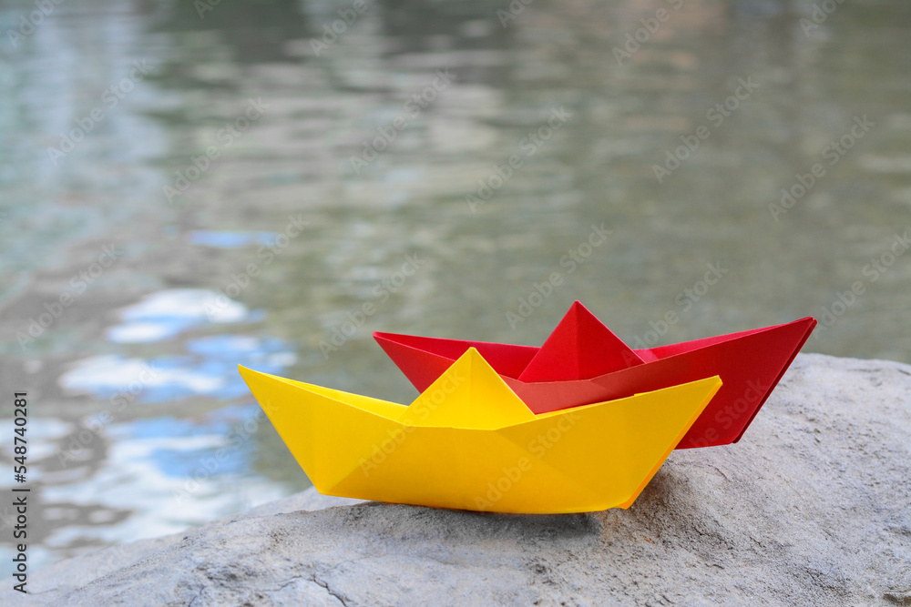 Beautiful yellow and red paper boats on stone near water outdoors