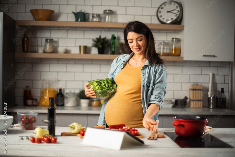 Beautiful pregnant woman preparing delicious food. Smiling woman preparing delicious food.
