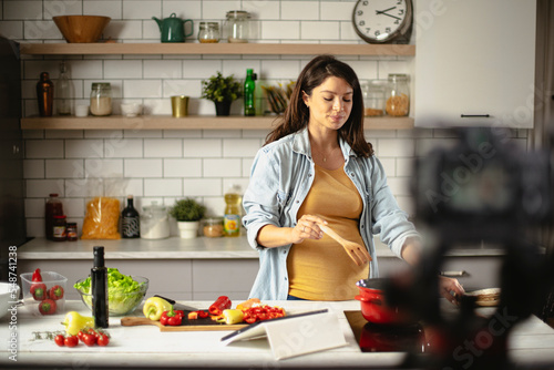 Beautiful pregnant woman filming cooking vlog. Happy woman filming her blog about healthy food at home.