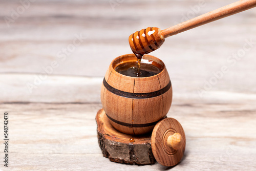 Honey dripping from honey dripper in a wooden barrel