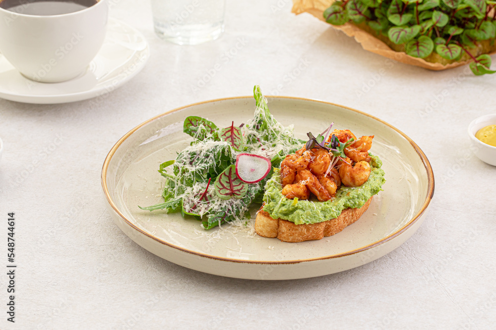 Portion of avocado toast with grilled shrimp and salad