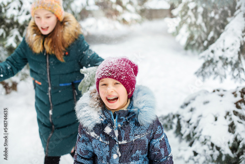 Two happy girls are having fun and throws first snow on background of forest. Children play outdoors in snow. Outdoor fun for family Christmas vacation