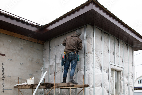 A man installs metal supports on the walls of the house for siding © schankz