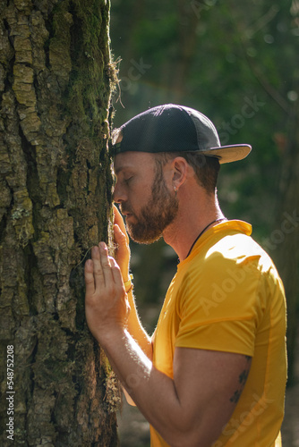 Hombre relajado en un bosque apoyado en un árbol con los ojos cerrados.