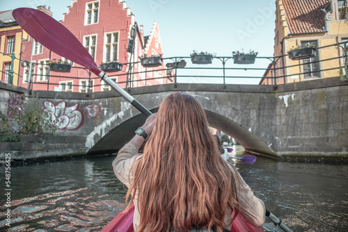Woman kayaking in the city Ghent, Belgium. Kayaking between buildings and trees.