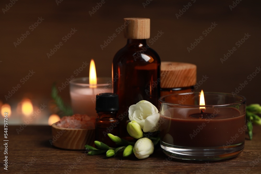 Beautiful spa composition with burning candles, different care products and flowers on wooden table