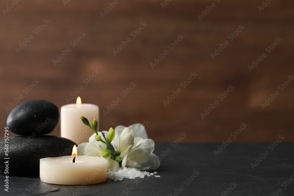 Beautiful composition with spa stones, burning candles and flowers on black table. Space for text