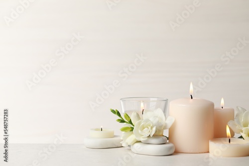 Beautiful composition with burning candles, spa stones and flowers on white table. Space for text