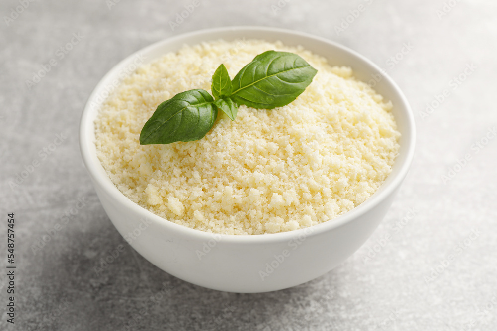 Bowl with grated parmesan cheese and basil on grey table, closeup Bowl with grated parmesan cheese and basil on grey table, closeup