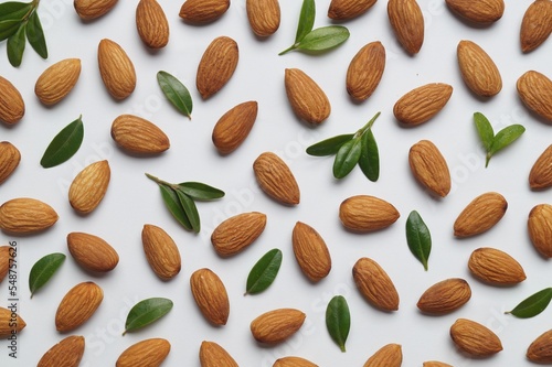 Delicious almonds and fresh leaves on white background, flat lay