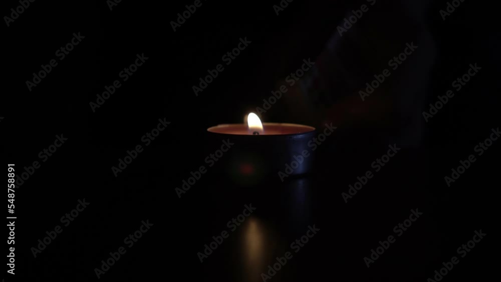 A man lights a candle with a match in the dark. Burning candle close-up in a dark room A man lights a candle with a match in the dark. Burning candle close-up in a dark room