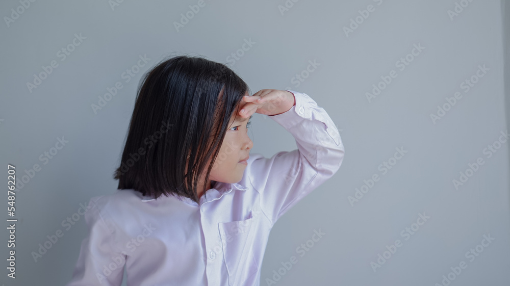 looking far away while hand on forehead. asian child isolated on light grey background. looking far away while hand on forehead. asian child isolated on light grey background.