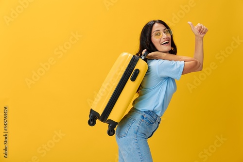 Traveler woman with yellow suitcase, passport and ticket in hand, paper plane, blue t-shirt and jeans on yellow background tourist, travel happiness, glasses, copy space