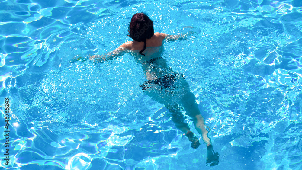 Woman in black bikini swims pool, top view.