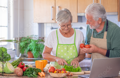 Attractive smiling senior couple working together in home kitchen preparing vegetables enjoying healthy eating. © luciano