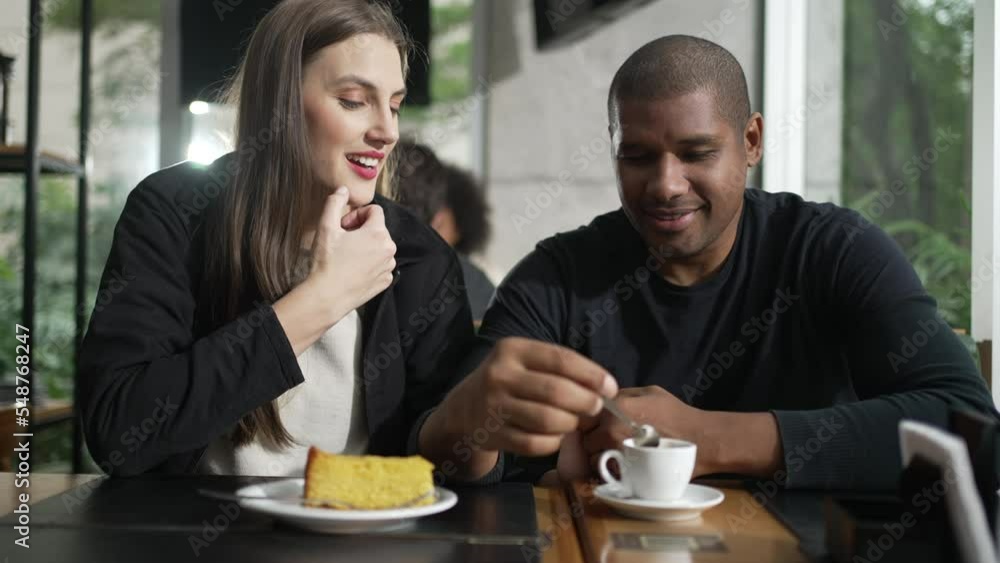 Happy couple seated at coffee shop talking. An interracial couple in conversation at cafe place restaurant. Two people smiling and laughing Happy couple seated at coffee shop talking. An interracial couple in conversation at cafe place restaurant. Two people smiling and laughing