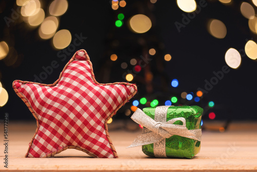 Green Christmas tgift box with a red checkered star shape on a wooden floor with Christmas lights bokeh
