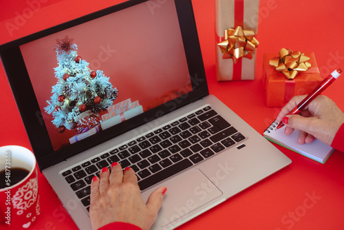 Woman's hands typing on laptop keyboard  at Christmas time - red background with Christmas presents