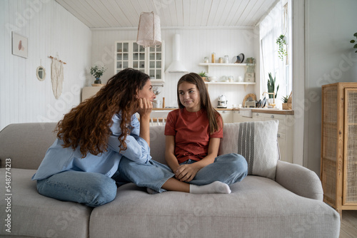 Teenage daughter sharing secrets with young loving supportive mother, parent mom talking chatting with adolescent girl while sitting together on sofa at home. Healthy parent-teen relationships photo