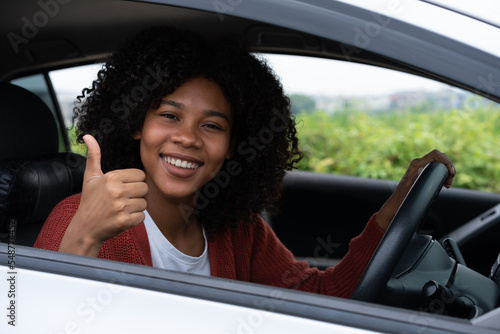 Young woman half asian half African shows thumb up inside of new modern car. Young woman excitement first road trip after pass drivers license test. Feels good after getting a new car.