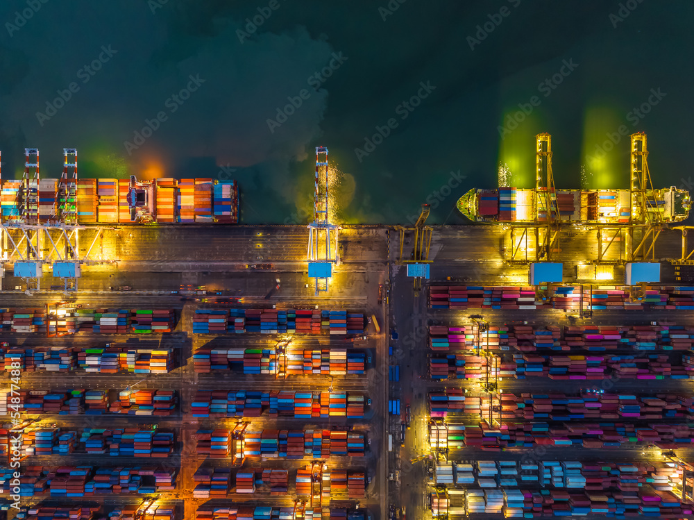 commercial port loading and unloading cargo from container ship import and export by crane for distributing goods by trailers transported to customers and dealers, twilght aerial view
