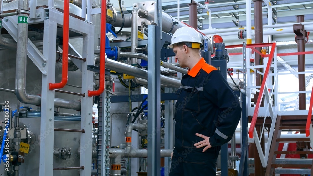 An engineer in a white helmet and overalls checks the operation of compressor equipment at the plant. An engineer inspects industrial equipment. Working at a gas liquefaction plant. An engineer in a white helmet and overalls checks the operation of compressor equipment at the plant. An engineer inspects industrial equipment. Working at a gas liquefaction plant.