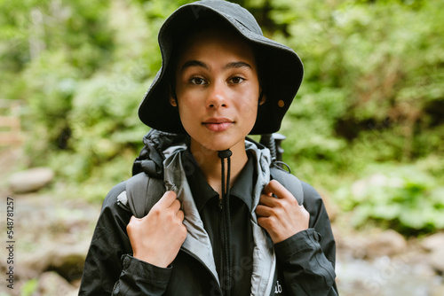 Happy white woman wearing backpack and panama hiking in forest
