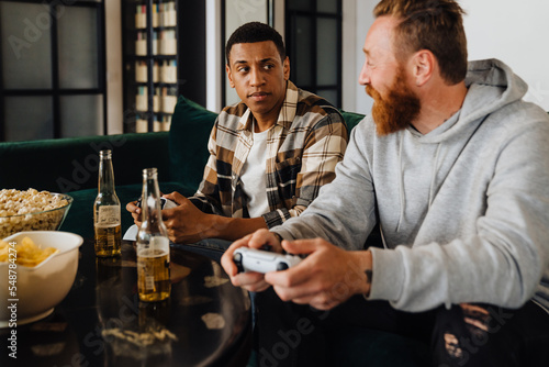 Two excited men playing video games and drinking beer in living room