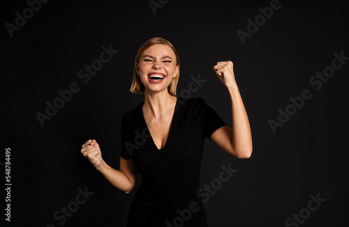 Cheerful woman with raised hands standing isolated over black background