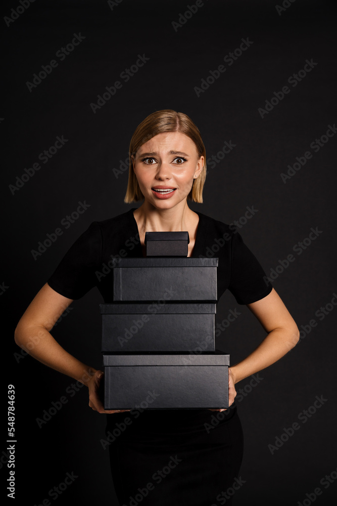 Confused woman holding gift boxes isolated over black background Confused woman holding gift boxes isolated over black background
