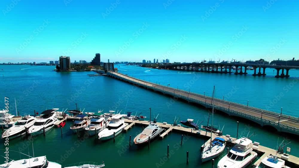 Aerial Shot Of Boats Moored In Sea By Bridge, Drone Moving Forward Over Marina During Sunny Day - Miami, Florida Aerial Shot Of Boats Moored In Sea By Bridge, Drone Moving Forward Over Marina During Sunny Day - Miami, Florida