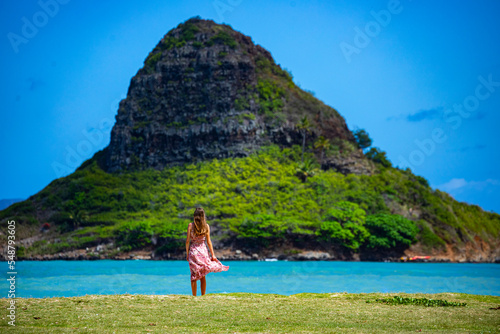 girl in long dress walks along seashore in kualoa regional park on oahu, hawaii, overlooking mokoli'i island with mighty mountain in background, holiday in hawaii islands photo