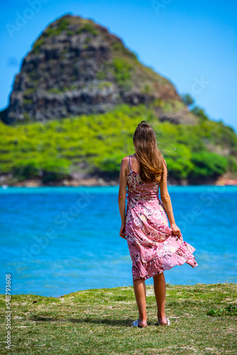 girl in long dress walks along seashore in kualoa regional park on oahu, hawaii, overlooking mokoli'i island with mighty mountain in background, holiday in hawaii islands photo