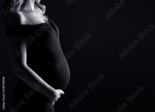 Beautifil silhouette of a pregnant woman with highlight on belly, woman in black, black and white photo, studio pregnancy shoot