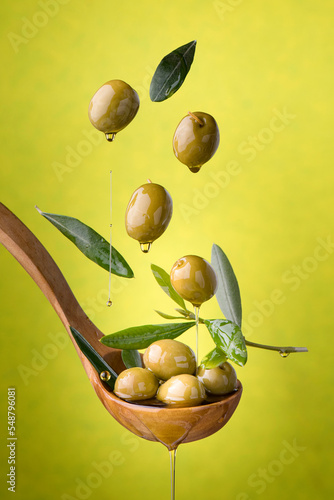 ladle with olives and oil on a green background. Olives, extra virgin olive oil and olive leaves float in the air photo