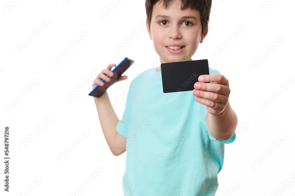 Selective focus on black credit card with blank space for your promotional text in the hands of a blurred teenage boy, smiling a cheerful toothy smile looking at camera, isolated over white background Selective focus on black credit card with blank space for your promotional text in the hands of a blurred teenage boy, smiling a cheerful toothy smile looking at camera, isolated over white background