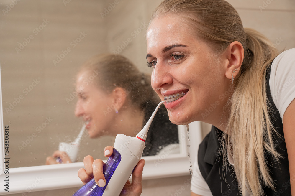 A woman with braces on her teeth uses an irrigator. Close-up portrait. A woman with braces on her teeth uses an irrigator. Close-up portrait.