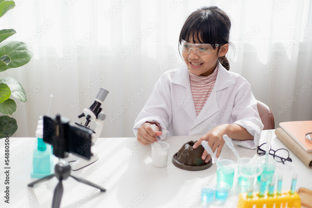 Asian school girl making easy chemistry experiments and recording a video for his followers, Young blogger kid posing in front of camera for vlog, Children make vlog for social media channel concept. Asian school girl making easy chemistry experiments and recording a video for his followers, Young blogger kid posing in front of camera for vlog, Children make vlog for social media channel concept.