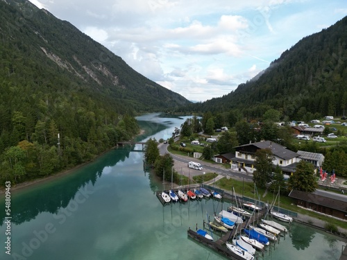 Lake in Tyrol Austria clear still water early morning row of moored boats drone aerial view .