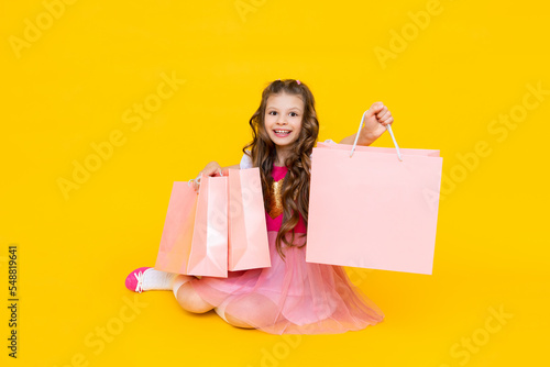 Happy child with packages after shopping. The little girl is very happy about new purchases. Sale of children's clothing. Gifts for a little princess on a yellow isolated background.