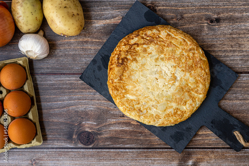 Top view, still life. Spanish potato omelette with some ingredients, on a wooden background.