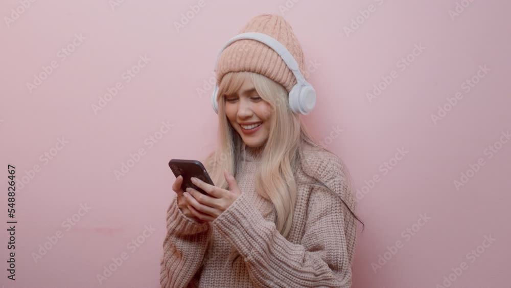 Portrait of Caucasian young woman wearing sweater using headphones over pink background.. Portrait of Caucasian young woman wearing sweater using headphones over pink background..