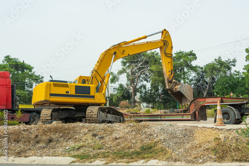 Crawler excavator, side view digs into a trench, next to a cargo trailer.