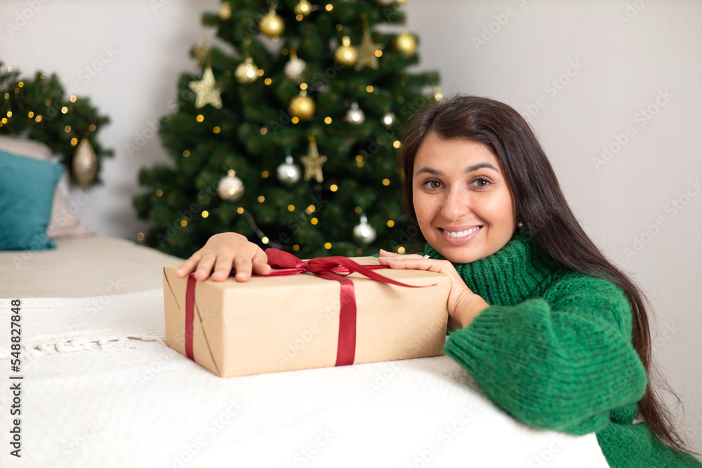 Merry Christmas. Portrait of a beautiful young woman in a cozy bedroom with a decorated Christmas tree in the background. Green sweater. Lifestyle Merry Christmas. Portrait of a beautiful young woman in a cozy bedroom with a decorated Christmas tree in the background. Green sweater. Lifestyle