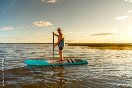 a man in shorts with a paddle on a sup board at sunset in the lake.