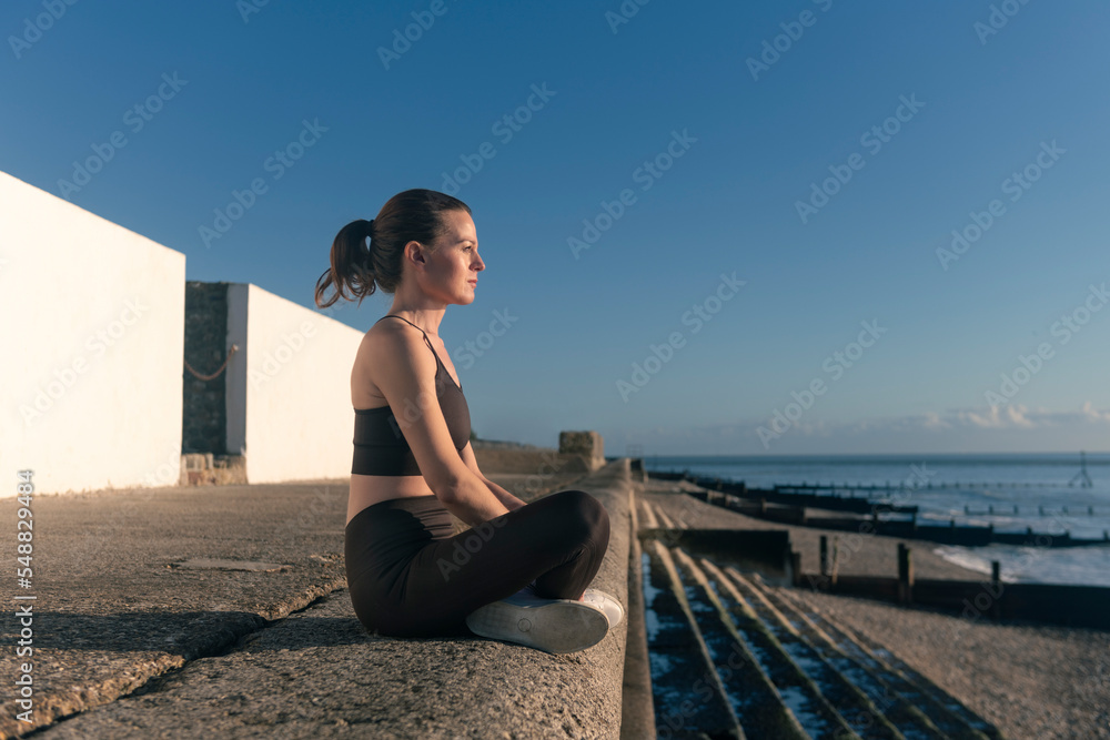 Woman sitting by the sea enjoying the evening sun. Health and wellness concept. Woman sitting by the sea enjoying the evening sun. Health and wellness concept.